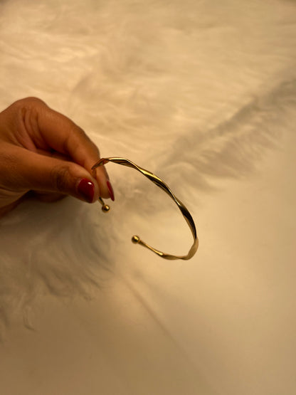 Gold bangle held by a hand with red nail polish against a neutral background