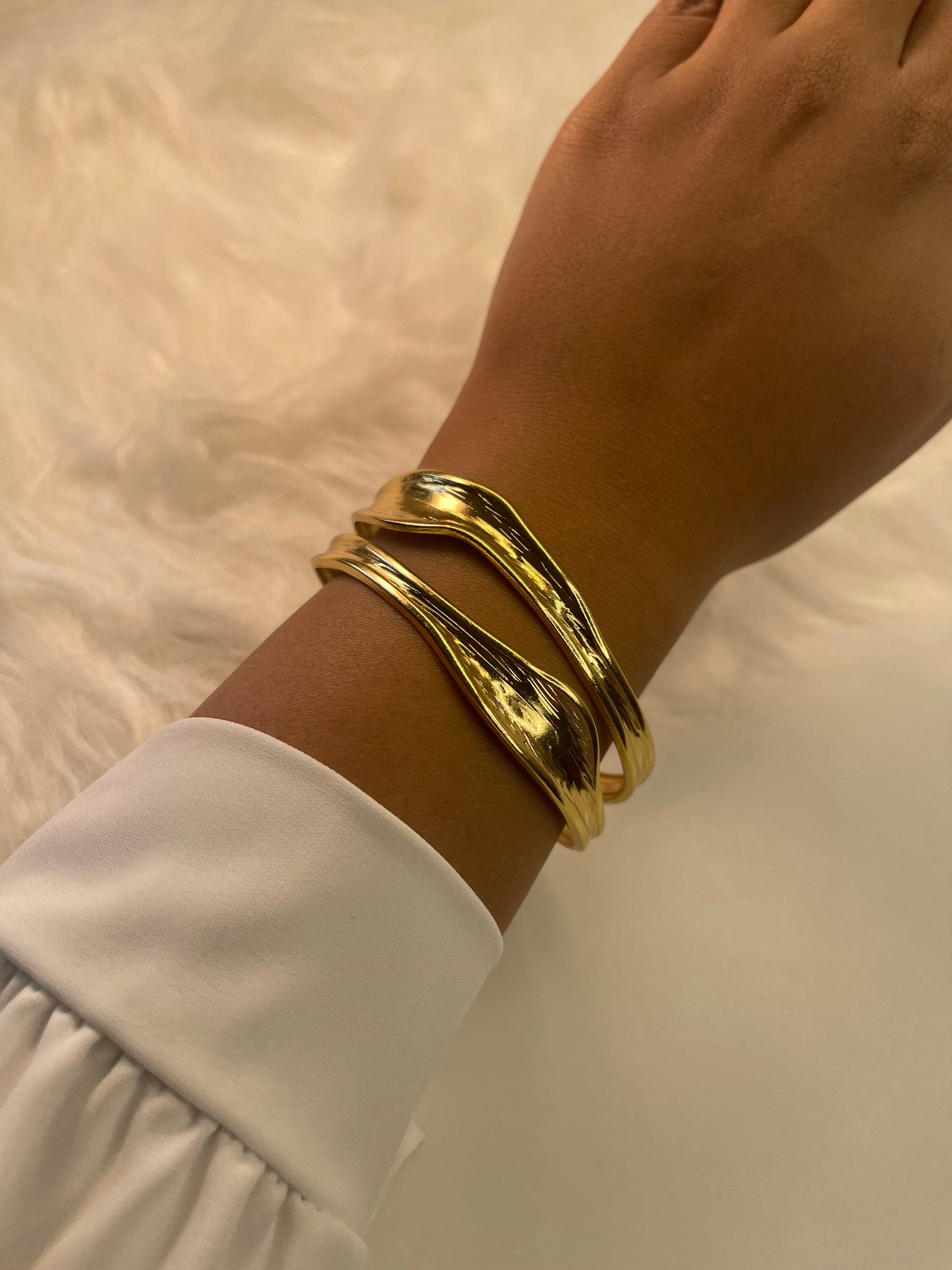 Gold bracelet on a wrist with a white sleeve against a neutral background