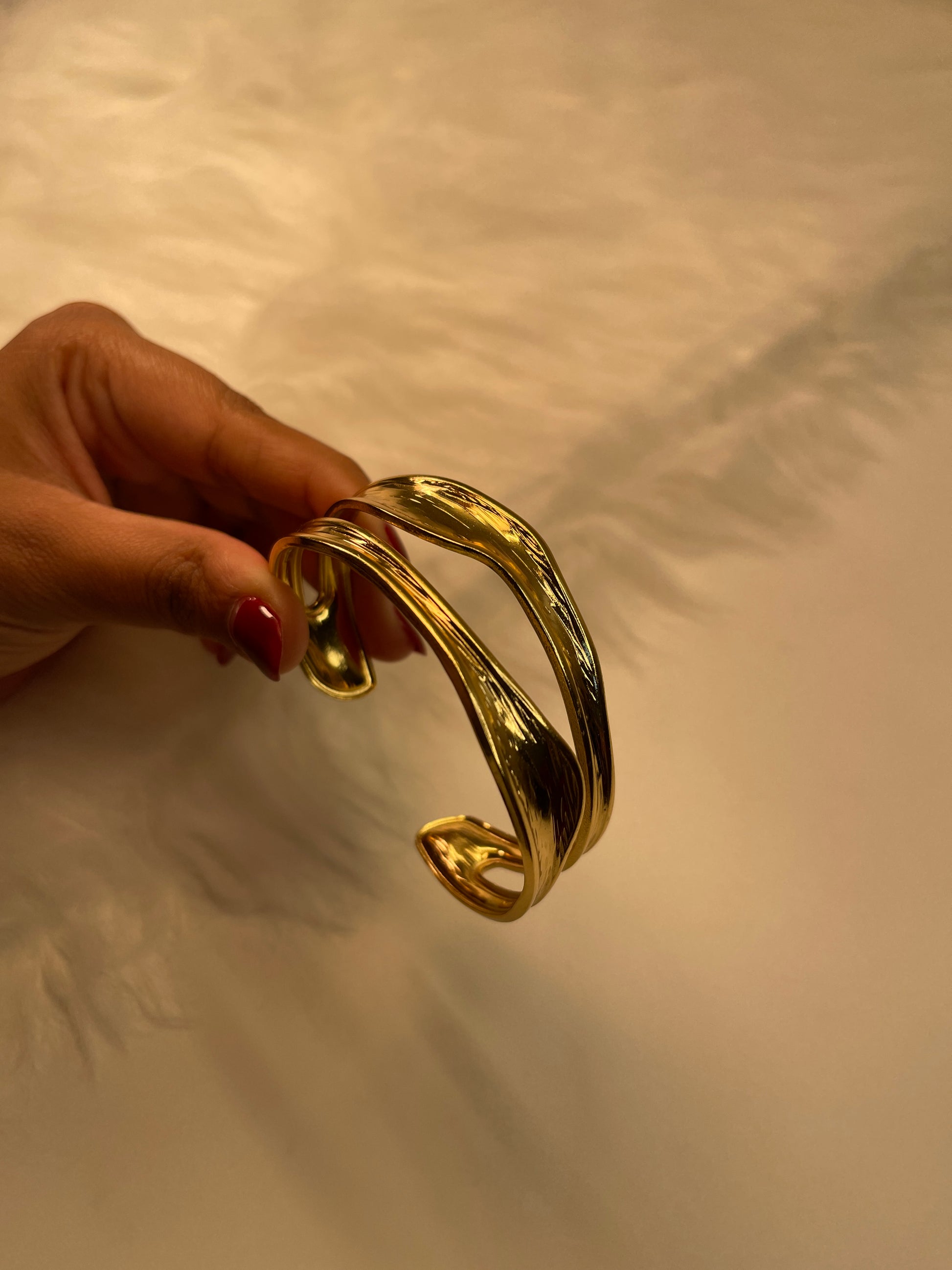 Gold bracelet held by a hand against a neutral background