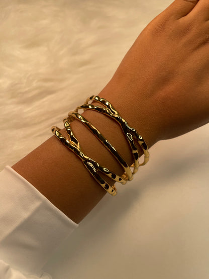 Gold bracelets on a wrist with a neutral background