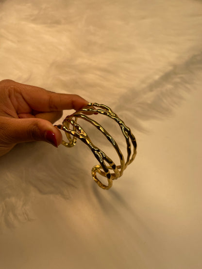 Gold bracelets held by a hand against a neutral background