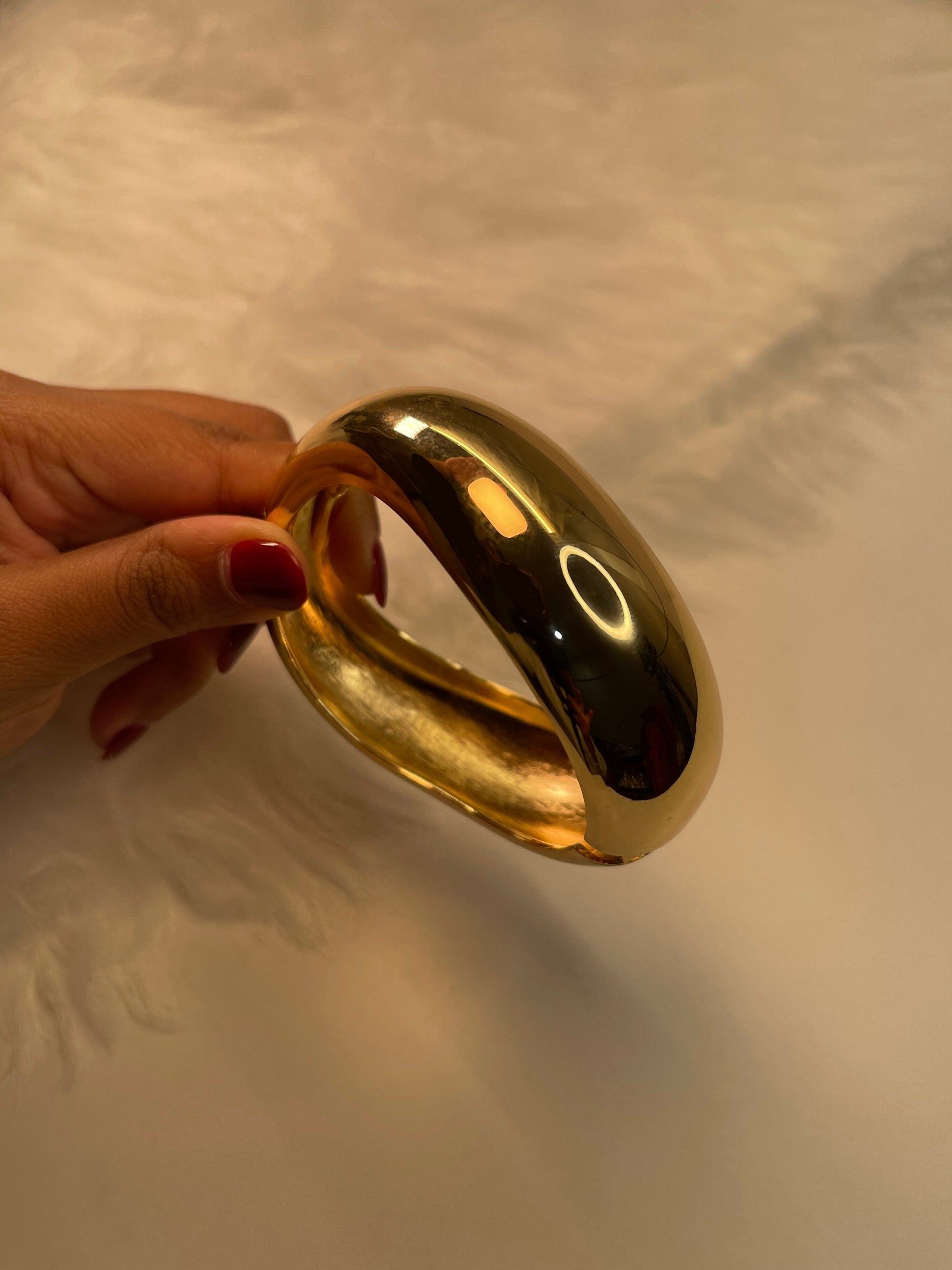 Wave Cuff Gold Bracelet held by a hand with red nail polish on a neutral background