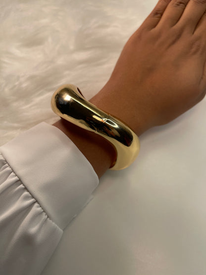 Gold bracelet on a wrist with a white sleeve against a neutral background