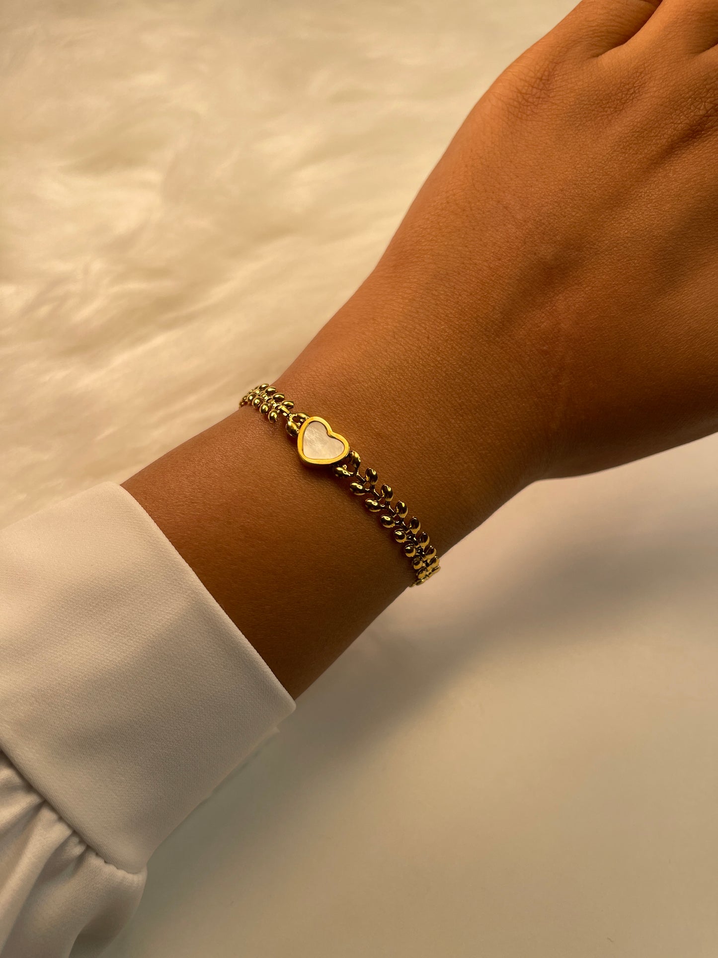 Gold bracelet with a heart charm on a wrist against a neutral background