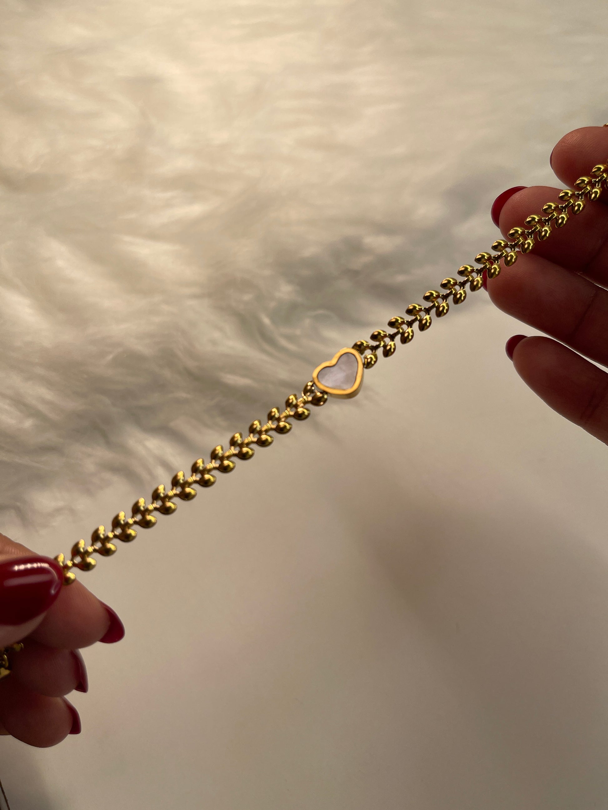 Gold bracelet with a white pendant held by a hand against a neutral background